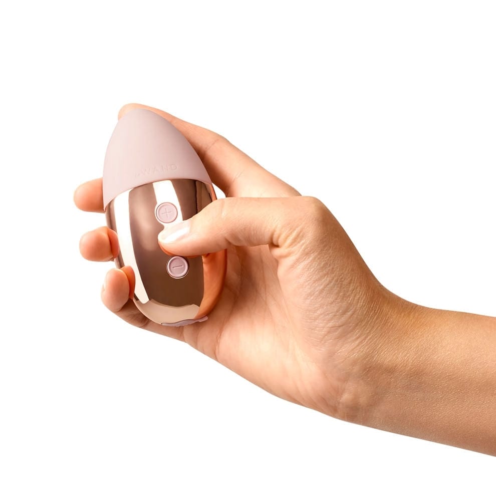 A woman's hand holding a shiny gold object with a pale pink pointed end that almost fits into the palm of her hand.